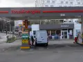 Station TotalEnergies avec une camionnette blanche en cours de ravitaillement. Panneaux de prix et de services.