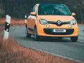 Une Twingo orange roule sur une route sinueuse bordée d'herbes sèches.