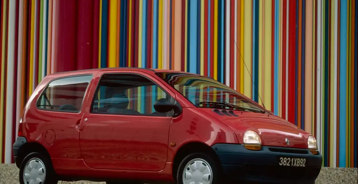 Renault Twingo 1 rouge devant un mur de bandes colorées verticales.