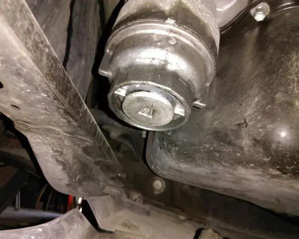 Filtre à huile de voiture sous le véhicule, avec une clé carrée insérée.