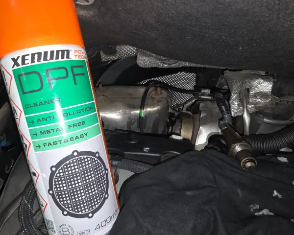 Bouteille de nettoyant FAP Xenum à côté d'un capteur et de pièces de moteur.
