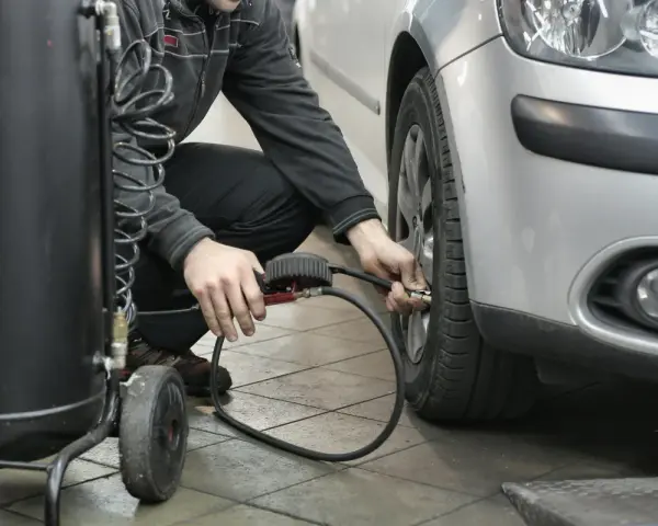 Un homme gonfle un pneu de voiture avec un manomètre et un compresseur.