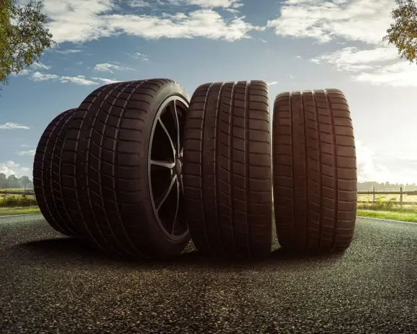 Trois pneus de voiture sur une route, avec un ciel nuageux et des arbres.
