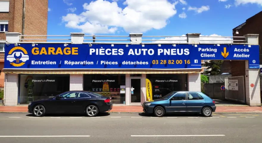 Garage avec enseigne bleue et jaune, deux voitures garées devant, sous un ciel bleu avec des nuages.